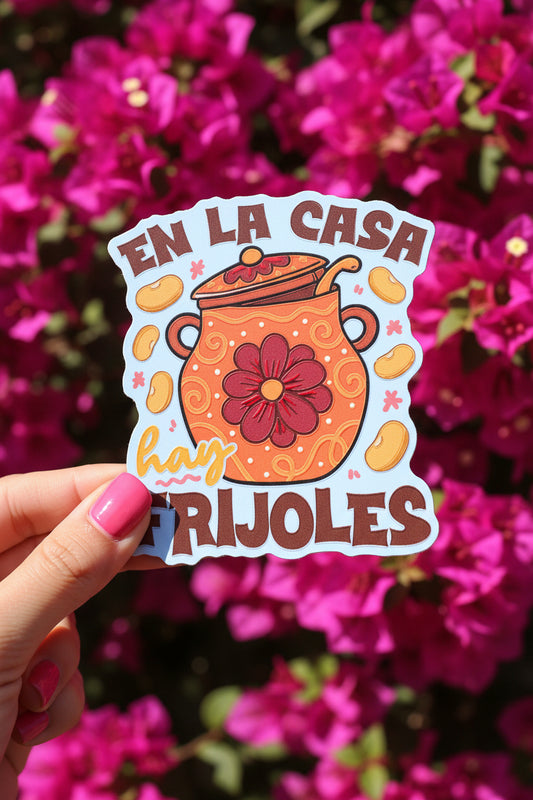 A colorful embroidered patch with the Spanish text 'EN LA CASA hay FRIJOLES' surrounding an orange pot with a dark red flower motif, set against a yellow background.