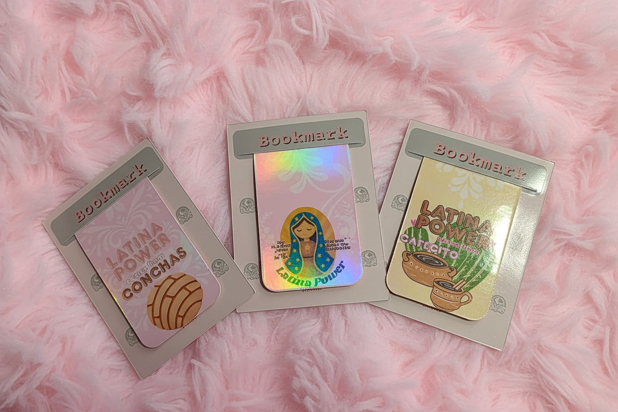 Three small printed bookmarks or cards laid on a light gray surface. The left card is pale pink with the words 'LATINA POWER' and a gourd illustration.