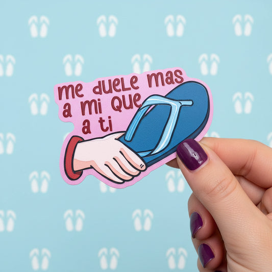 A die-cut sticker' featuring a pink background with the Spanish text 'me duele mas a mi que a ti' in dark red letters, alongside an illustration of a hand holding a blue flip-flop sandal with a light blue strap. The patch is displayed on a solid yellow background.